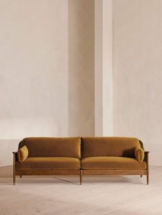 a brown couch sitting on top of a wooden floor next to a white wall in an empty room