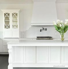 a kitchen with white cabinets and flowers on the counter top in front of an oven