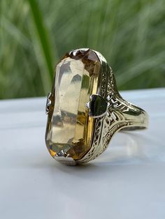 This is a lovely vintage Topaz cocktail ring, and what a darlin' she is. An 18k yellow gold band/setting with thick white gold prongs. The band features very organic, art nouveau-ish detailing. The Topaz is a smokey goldish color, which pairs beautifully with the colors in the band. Oh, that big ol' Topaz is 22 x 11mm. KAPOW! Please view the video for minor surface scratches to the topaz that are visible when viewing closely at certain angles. Not exceptionally noticeable. Details: Metal Purity Luxury Yellow Gold Topaz Ring In Art Deco Style, Luxury Unique Yellow Gold Topaz Ring, Luxury Vintage Topaz Ring Collectible, Vintage Luxury Topaz Ring Collectible, Luxury Yellow Gold Topaz Ring, Classic Yellow Gold Rings With High Luster, Classic Yellow Topaz Ring With Emerald Cut, Classic Yellow Emerald Cut Topaz Ring, Classic Emerald Cut Yellow Topaz Ring