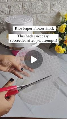 a person cutting paper with scissors on top of a table next to flowers and cake