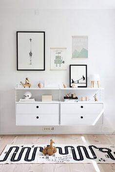 a white room with black and white pictures on the wall, wooden flooring and drawers