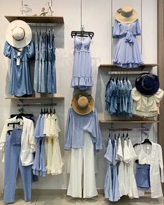 clothes and hats are hanging on shelves in a clothing store, including blue shirts and white pants