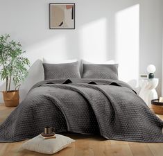 a bed in a room with white walls and wooden flooring that has a gray comforter on it