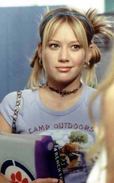 a woman holding a book in her hand and looking at the camera with a serious look on her face