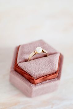 an engagement ring sits on top of a pink velvet box that is sitting on a table