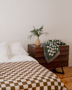 a bed sitting next to a nightstand with a vase on top of it and a checkered blanket