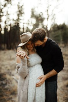 a pregnant couple cuddling in the woods