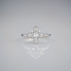 an engagement ring with a princess cut diamond in the center, on a reflective surface