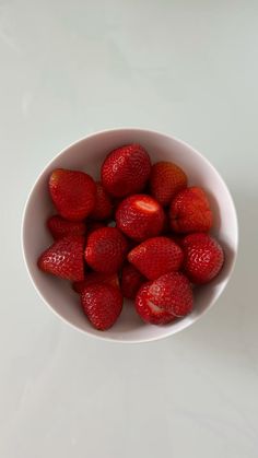 a white bowl filled with lots of ripe strawberries on top of a white table