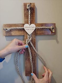 two hands holding a cross with a heart on it and rope attached to the cross