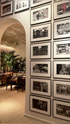 a wall full of black and white photos in a room with arched doorway leading into the dining area