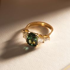 a green ring with three baguets on it sitting on a white table top