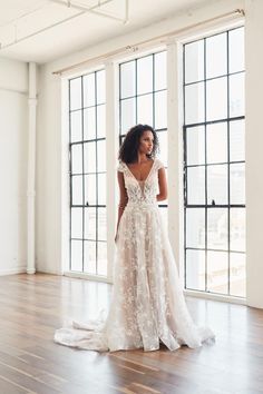 a woman in a white wedding dress standing on a wooden floor next to large windows