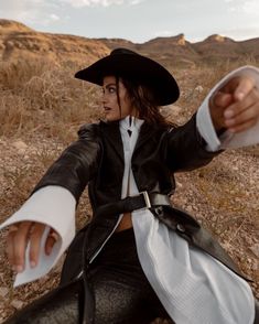 a woman dressed in black and white is sitting on the ground with her arms outstretched