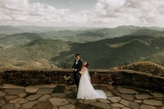 a bride and groom standing on top of a mountain