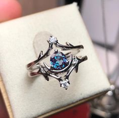 a ring with an oval blue stone surrounded by small white diamonds sits in a box