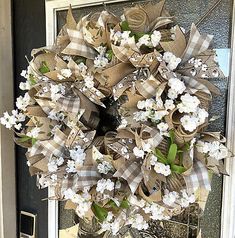 a wreath with white flowers and burlocks is hanging on the front door sill