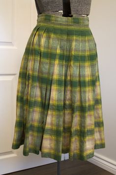 Just an absolutely gorgeous, classic 1950s circle skirt made of a substantial, quality wool fabric in shades of green, yellow, beige and tan. Pleated waist. Closes with two grey moonglow buttons and a small metal Lightning zipper. Forms a full circle. Falls to about mid-calf. No label, appears to have been homemade, but made very well. Condition: very good. It has one small hole on the back which I darned, see last photo. I am not the world's best seamstress, so you may prefer to redo it, but at Retro Green A-line Skirt, Vintage Full Skirt With Accordion Pleats, Green Accordion Pleats Skirt, Fitted Green Accordion Pleated Skirt, Vintage Plaid Full Skirt, Vintage Pleated Plaid Skirt, Retro Green Skirt For Fall, Vintage Fitted Green Skirt, Retro Green Pleated Skirt