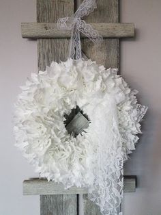 a white wreath hanging from the side of a wooden cross on top of a wall