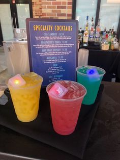 three different colored drinks sitting on top of a table next to a sign that says specialty cocktails