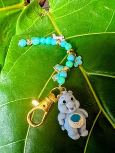 a keychain with an elephant charm hanging from it's side on a green leaf