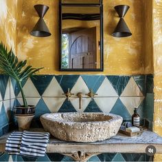 a bathroom sink sitting under a mirror next to a potted palm tree in front of it