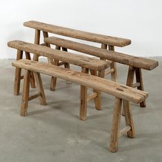 three wooden benches sitting next to each other on top of a cement floor in front of a white wall