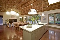 a large open kitchen and dining room with wood ceilinging, white counter tops and wooden beams