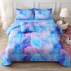 a bed covered in blue and pink galaxy comforter sets with pillows on the side