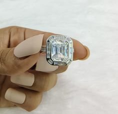 a woman's hand holding a ring with an emerald stone in the center and two diamonds on each side