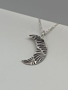 This unique silver moon necklace has been entirely handmade using .999 fine silver. It has been cut from fine silver precious metal clay, textured, fired and oxidized. The pendant hangs from a sterling silver diamond cut cable chain. This fine silver pendant features an embossed leaf print pattern and hangs 7/8 inches from top of ring to bottom of the moon shape. Pendant size: approximately 5/8 x 1/2 inches Chain length: adjustable at 16 and 18 inches can also be customized to whatever length ne Unique Etched Sterling Silver Necklace, Unique Silver Etched Necklaces, Handmade Crescent Sterling Silver Jewelry, Bohemian Moon Phase Necklace In Sterling Silver, Bohemian Sterling Silver Moon Phase Necklace, Artisan Silver Necklace With Moon Phase, Bohemian Silver Necklace With Moon Phase, Artisan Silver Necklace With Moon Phase Detail, Artisan Silver Necklace With Moon Charm