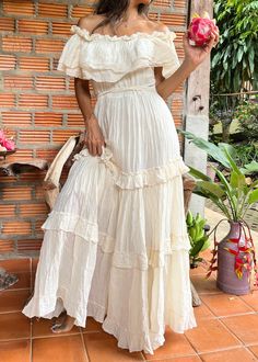 a woman in a white dress is holding a pink flower and posing for the camera