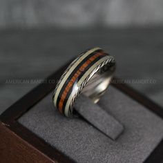 a silver ring with wood inlays sits on top of a wooden box and is ready to be worn