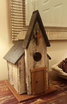 a birdhouse with a cross on the top and a bowl of pine cones below