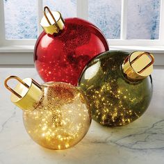 three christmas ornaments sitting on top of a marble counter next to a window with snow outside