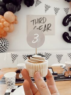 a person holding up a cupcake with a number 3 on it in front of some black and white balloons