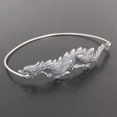 "Dragon Bangle Bracelet. A silver tone dragon charm will be transformed into a dragon bangle bracelet with bangle band choice of silver filled or sterling silver. This Chinese New Year bracelet also comes in gold tone with a brass or 14k gold filled bangle band. Personalize your dragon bracelet with custom initial charms or birthstone charms to create a customized dragon charm bracelet; http://www.etsy.com/shop/FrostedWillow?section_id=6596366 Please specify size in notes to seller during checko Adjustable Sterling Silver Dragon Jewelry, Adjustable Sterling Silver Jewelry With Dragon Design, Silver Symbolic Charm Bangle Bracelet, Symbolic Silver Bangle Charm Bracelet, Mystical Dragon, Chinese Bracelet, Chinese New Year Gift, Chinese New Year Gifts, Dragon Bracelet