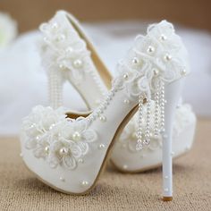 a pair of white high heeled shoes with pearls