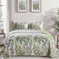 a bed covered in green and white comforter next to two pictures on the wall