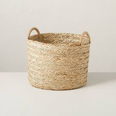 a large woven basket with handles on the top and bottom, sitting on a white surface