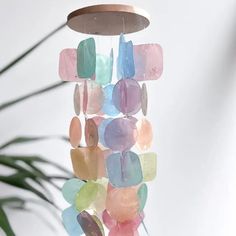 a wind chime made out of sea glass and wood with a plant in the background