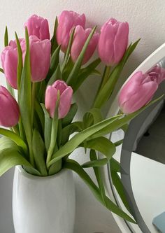 pink tulips in a white vase sitting on a table next to a mirror