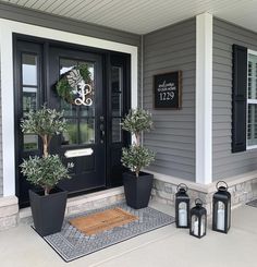 two potted plants sit on the front porch of a gray house with black doors