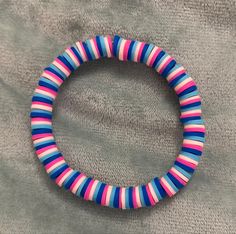 a pink, blue and white beaded bracelet on a gray cloth with a black clasp