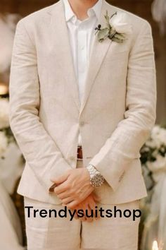 a man in a white suit and flower boutonniere standing next to a table