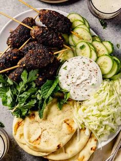 a white plate topped with meat and veggies next to pita breads