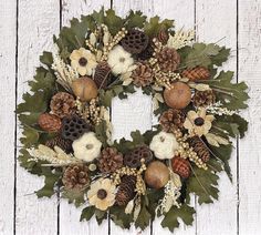 a wreath with pine cones, acorns and leaves on a white wooden background