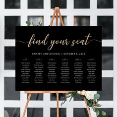 a black and white wedding seating sign with greenery on it, next to a wooden easer