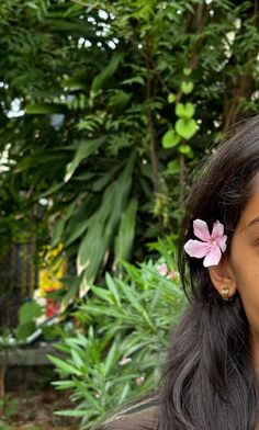 a close up of a person with a flower in her hair and some plants behind her