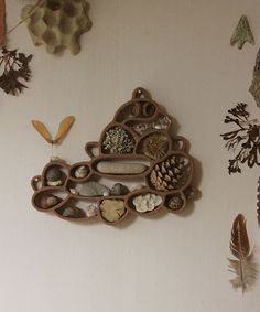 there is a clock made out of wood and shells on the wall next to feathers